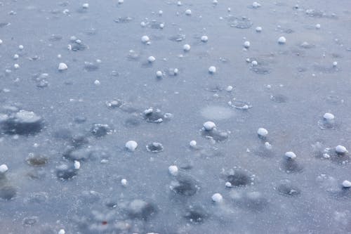 pexels-photo-8237250 Free Close-up view of frozen hailstones scattered on icy pavement, showcasing winter weather phenomena. Stock Photo