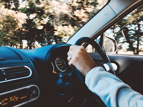 Free Driver's hand on steering wheel of a modern car during a daytime drive through scenic outdoors. Stock Photo