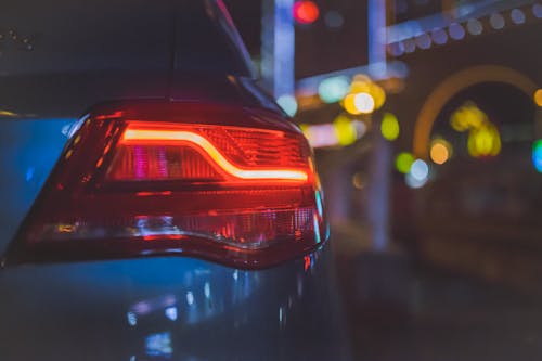 Free Close-up of a car's tail light with colorful bokeh background in an urban night setting. Stock Photo